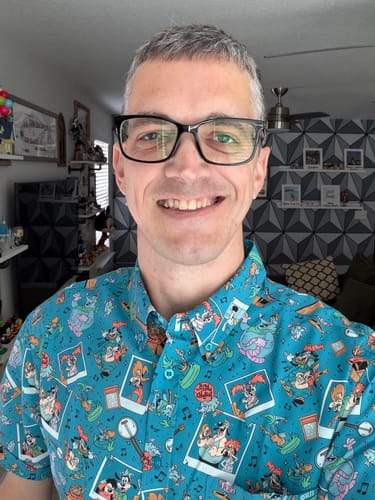 Reviewer smiling while wearing the teal, patterned "Lester's Possum Park" short sleeve shirt.