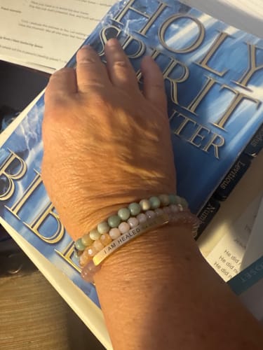 Customer's wrist wearing the 'I AM HEALED ISA 53:5' bracelet stacked with other beaded bracelets, resting on a Bible.