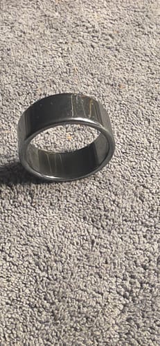 La bague hématite d'un client, un anneau large et brillant, posée sur un tissu gris.