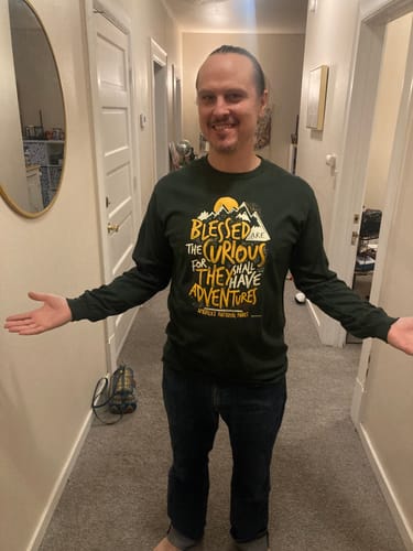 Reviewer smiling while wearing the green Blessed Are The Curious Long Sleeve Tee in a hallway.