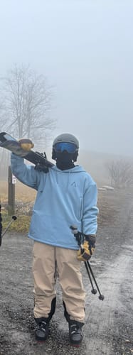 Reviewer wearing the baggy Timber Tan Insulated Snow Pants outdoors on a foggy day, holding skis.