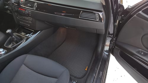 Klient pokazuje czarny, dopasowany dywanik samochodowy zainstalowany po stronie pasażera w samochodzie.