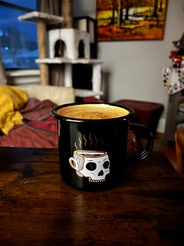 Customer's black Double Depresso Mug with a skull graphic, filled with coffee and sitting on a wooden table.