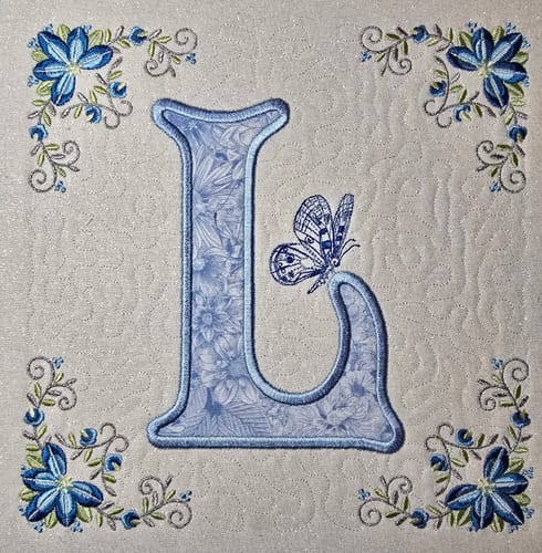 Customer's quilted square using the Flowers & Butterflies Fabric for an appliquéd letter 'L' with blue embroidered flowers.