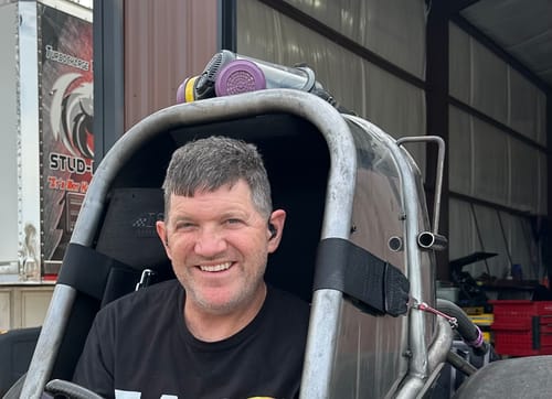 Reviewer smiling in a race car cockpit while wearing black GS Extreme 3.0 hearing protection earbuds.