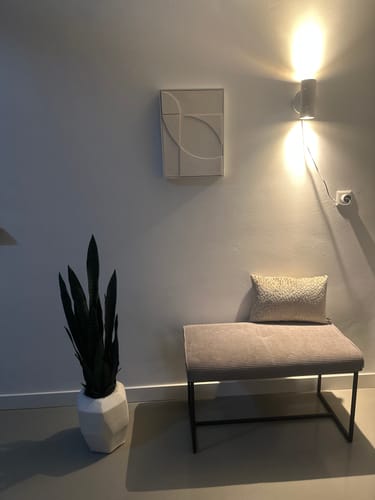Recensent toont de witte Wandlamp Tivoli die sfeervol licht geeft op de muur.