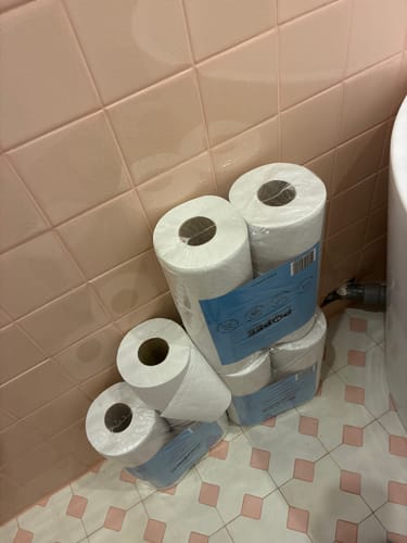 Client montrant plusieurs paquets de PAPIER TOILETTE Compact empilés dans une salle de bain rose.