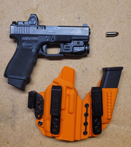 Customer's orange AXIS ELITE holster laid out next to a handgun with an attached light and optic.