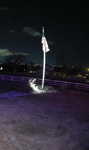 Reviewer's American Flag on a flagpole at night, brightly illuminated by a spotlight from below.