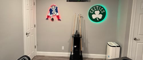 Reviewer's Boston Celtics Shamrock wall art with green backlighting, displayed on a game room wall.