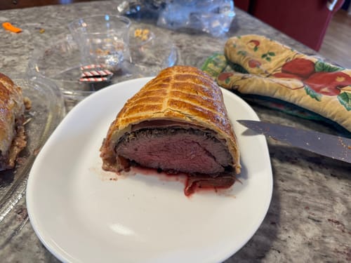 Customer's Beef Tenderloin prepared as a golden Beef Wellington, sliced to show the tender pink meat inside.