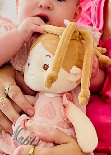 Reviewer's baby holding the soft Personalized Sweetheart Girl doll. The doll is wearing a pink dress with a heart pattern.