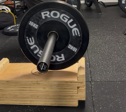 Customer's two stacked Premium Wooden Deadlift Blocks supporting a barbell with weights in a gym.