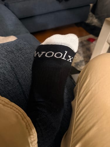Customer's foot wearing the black Mens Core Crew Sock with a white toe, showing the 'woolx' logo.