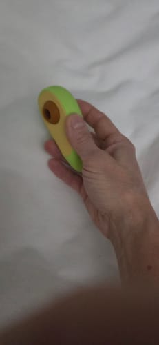 A customer's hand holding the green Avo Clitoral Massager against a white fabric background.