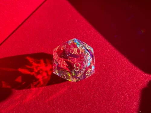 Customer's close-up of a URWizards prism glass d20 die on a red tray, casting a colorful light reflection.
