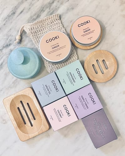 Reviewer's collection of colorful Hand & Body Soap boxes, bamboo soap dishes, and other products on a marble counter.