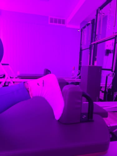 Close-up of a reviewer's Sunkissed grip socks on pilates equipment in a purple-lit studio.