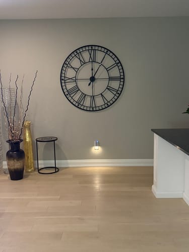 Customer's large black Roman numeral wall clock mounted on a light-colored wall in their home.