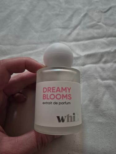 Customer holding the small frosted glass bottle of Dreamy Blooms perfume against a light fabric background.