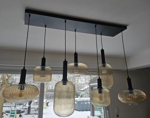 Klant toont de gemonteerde Lucide Maloto hanglamp met amberkleurige, geribbelde kappen.