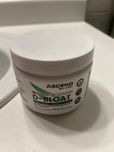 Customer's white tub of D-BLOAT Strawberry Kiwi powder supplement on a bathroom countertop.