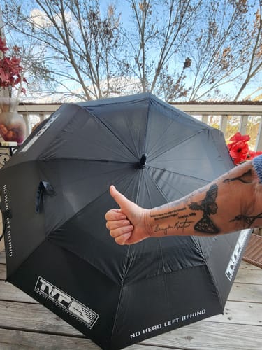 Customer gives a thumbs up in front of their large T.V.P. Umbrella, showing the "NO HERO LEFT BEHIND" text.