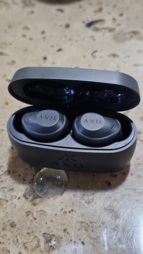 Reviewer's black XCOR PRO earbuds sitting inside their open charging case on a counter.