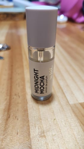 Customer's bottle of Midnight Mocha perfume standing upright on a wooden surface.