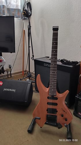 Ein Kunde zeigt die Donner NHL-500 Headless E-Gitarre auf einem Ständer in einem Übungsraum.