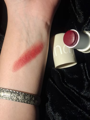 Customer's arm showing a swatch of the VELVET FLUSH Lip+Cheek Blush next to the open berry-red stick.