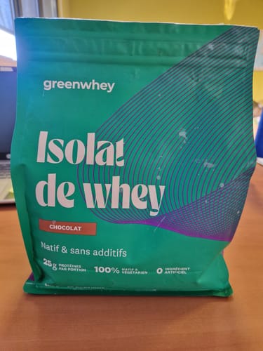Un client montre le sachet vert d'Isolat de Whey Native saveur chocolat sur une table.