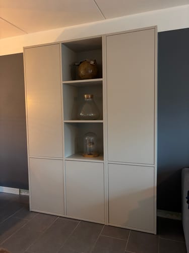 Recensent toont de grijze WOOOD Meggy opbergkast in een woonkamer.