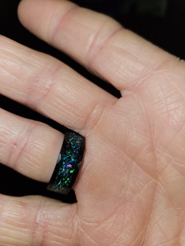 Close-up of a reviewer's hand wearing the black Astralis ring, showing the green and purple opal inlay.