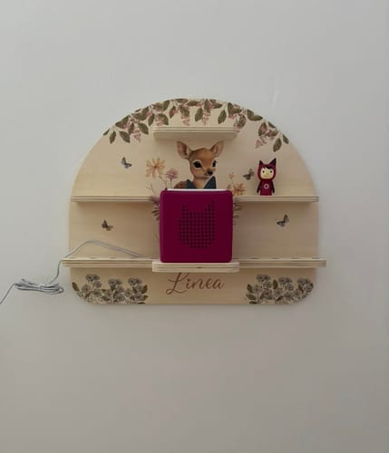 Rezensent zeigt das personalisierte Tonie-Regal „Linea“ mit Rehmotiv an einer Wand.