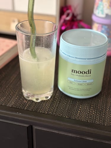 Customer's tub of Lemon Lime probiotic blend next to a prepared glass of the drink with a green straw.