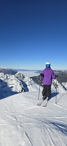 Customer in baggy waterproof snow pants standing on skis on a snowy mountain.