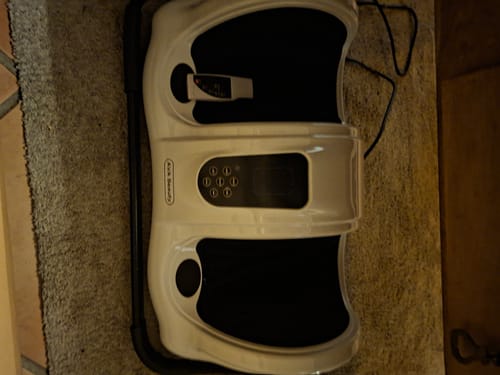 Anmelders hvide og sorte fod- og lægmassageapparat, der står på et gulvtæppe.