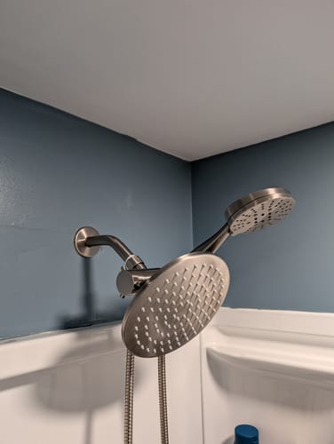 Reviewer's solid metal 3-Spray Dual Shower Head Set installed in their shower against a blue wall.