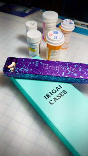 Customer's purple Weekly Case engraved with 'Gratitude', shown open with pills inside, next to its box and prescription bottles.