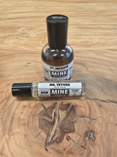 Recensore mostra il profumo MR. VETIVER in formato piccolo su un tavolo di legno, accanto a un'altra boccetta.