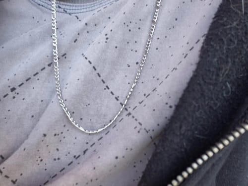 Primer plano de un cliente que lleva puesta la Cadena Fígaro 3mm plateada sobre una camiseta estampada.