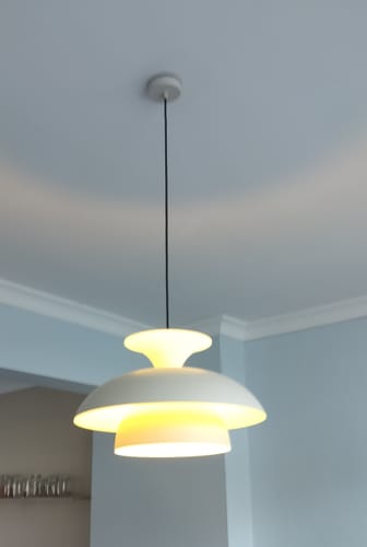 Recensent toont de verlichte beige Titus hanglamp, die elegant aan het plafond hangt.