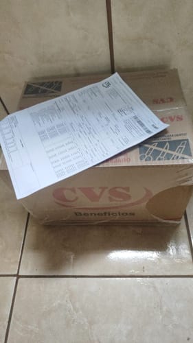 Caixa de papelão da Cesta de Natal Rubi do cliente, vista fechada com um documento em cima, em um piso de cerâmica.