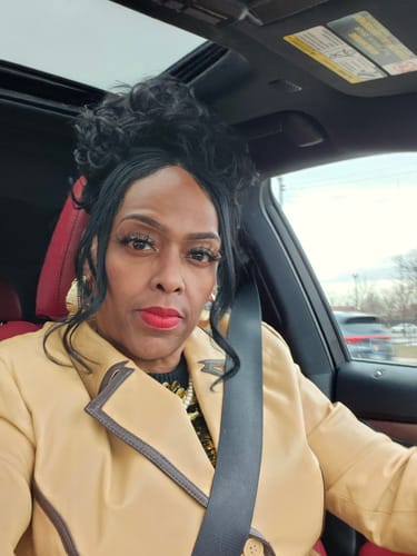 Reviewer in a car wearing the Vivica A Fox Bang N Pony piece styled as a curly black updo with bangs.