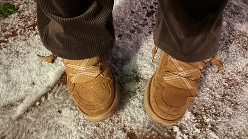Close-up van de UGG Lowmel Chestnut-schoenen van een recensent in de sneeuw.