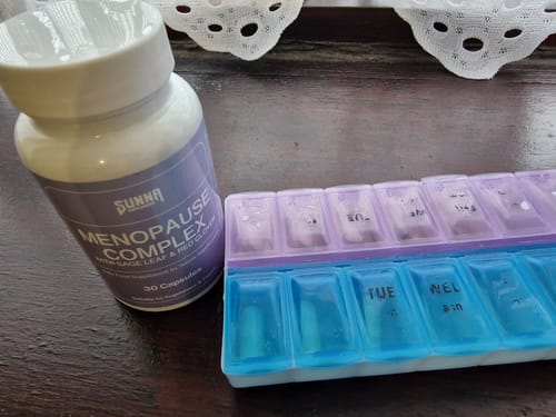 Reviewer's white bottle of Menopause Complex next to a purple and blue daily pill organizer.