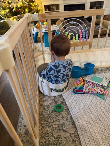 Reviewer's photo of a small child sitting inside the personalized white rope basket in a play area.