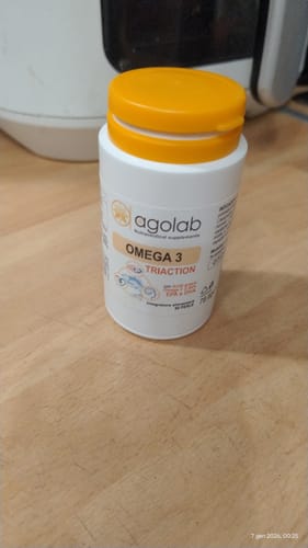 Recensore mostra il flacone di Omega 3 Tri-Action su un tavolo di legno.