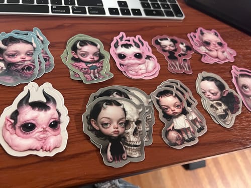 Customer's custom vinyl stickers showing various detailed, gothic-style characters spread out on a desk.